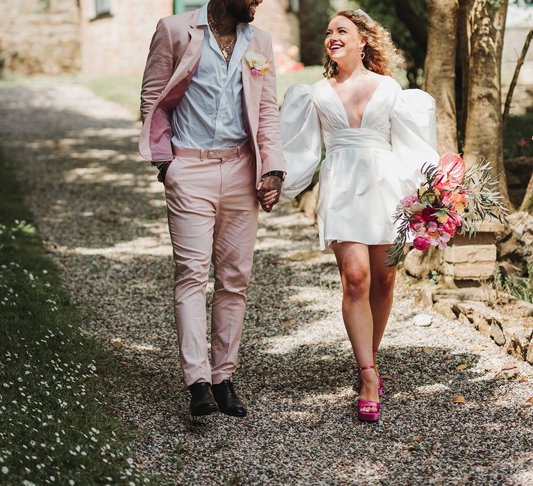 Bride with blonde curly hair walking holding hands with the from at their pink themed inspired day 