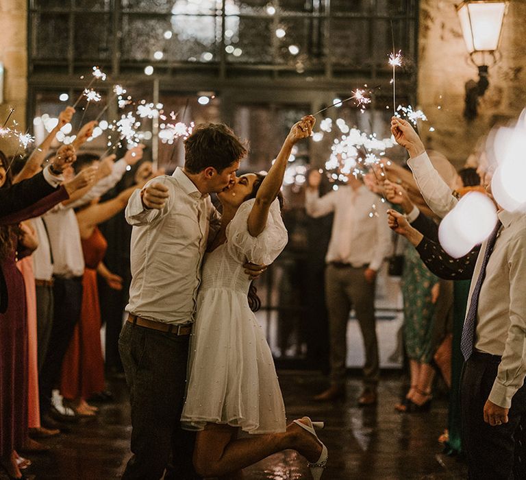 The bride and groom wave sparklers with their guests at the end of the wedding day 