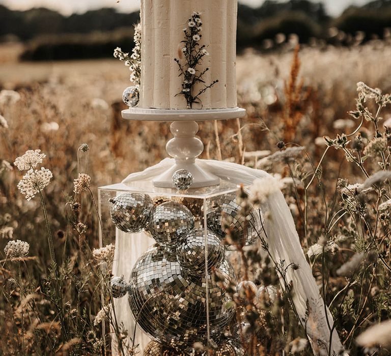 Two tier buttercream wedding cake decorated with wildflowers on a perspex cake stand with disco balls 