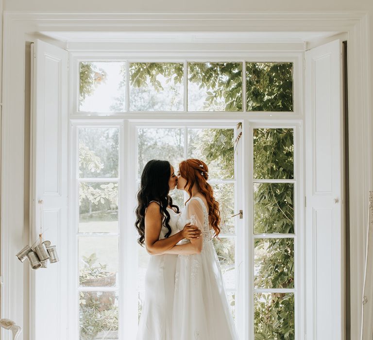 Two brides pose by window together for beautiful couple portrait at barn wedding 