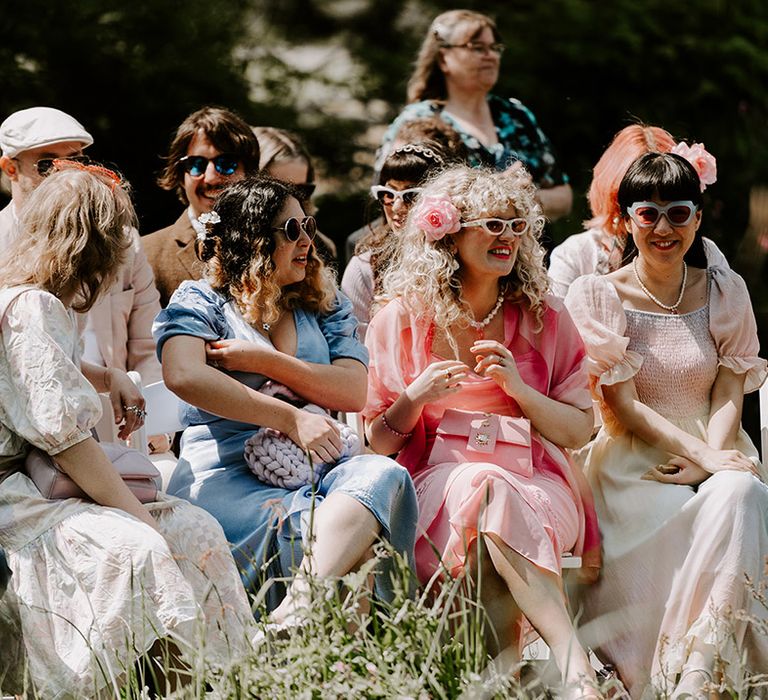 Wedding guests in pink, blue and green pastel wedding outfits seated for the wedding ceremony 