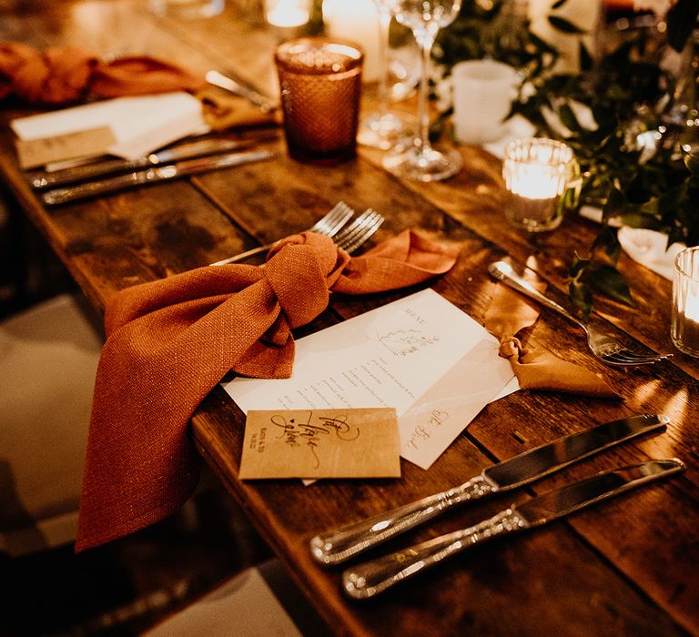 Warm toned autumnal wedding tablescape with an orange theme including orange napkins and white wedding stationery 