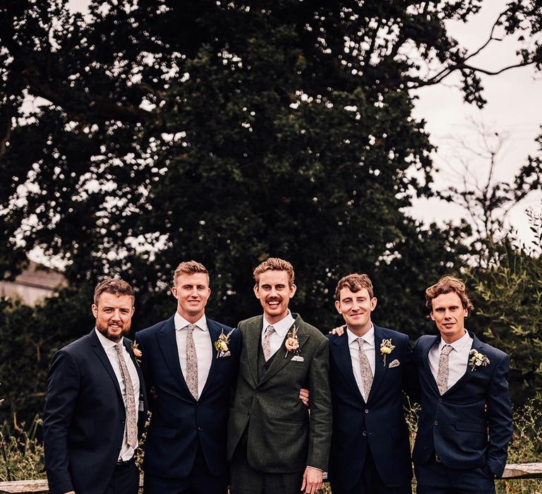 Groomsmen in navy suits posing with the groom in a dark green suit 