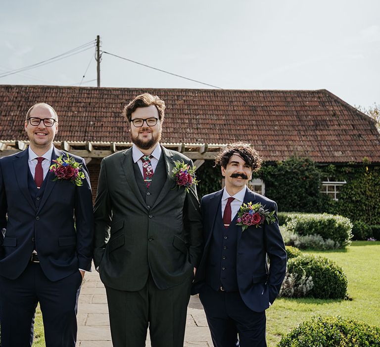 The groom and groomsmen stand together wearing oversized buttonholes 