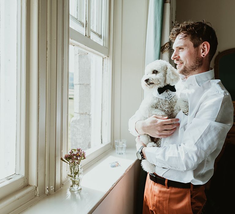 Groom with pet dog looking out the window as they get ready for the wedding 