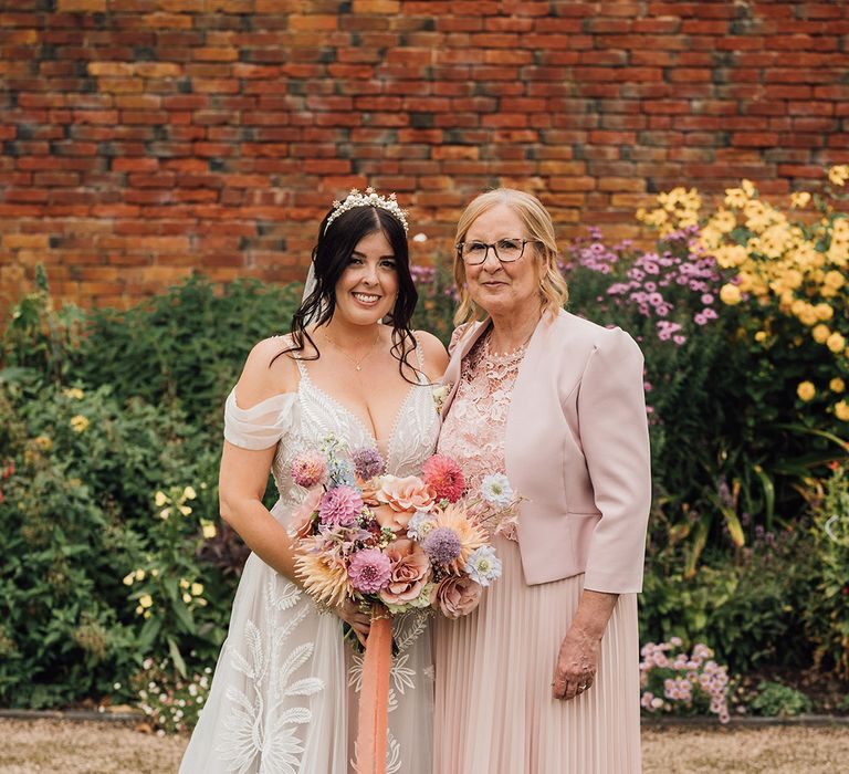 Bride in lace princess tulle wedding dress with colourful bouquet standing with mum in pink wedding outfit 