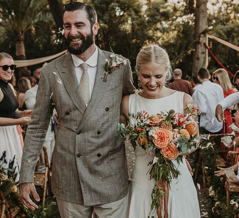 Bride holding a bouquet with coral flowers and groom wearing a double breasted jacket 