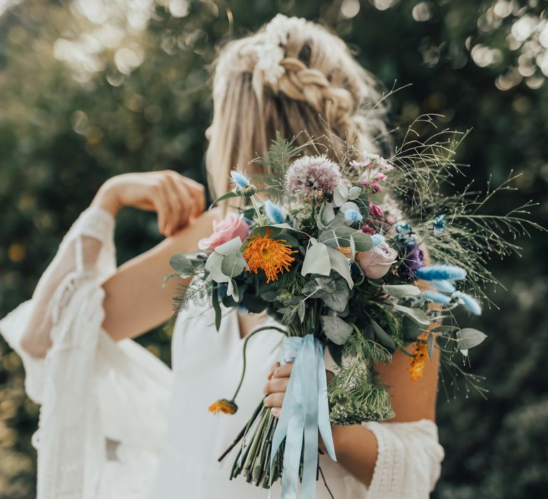 Bride holds bright and vibrant bouquet tied with light blue ribbon