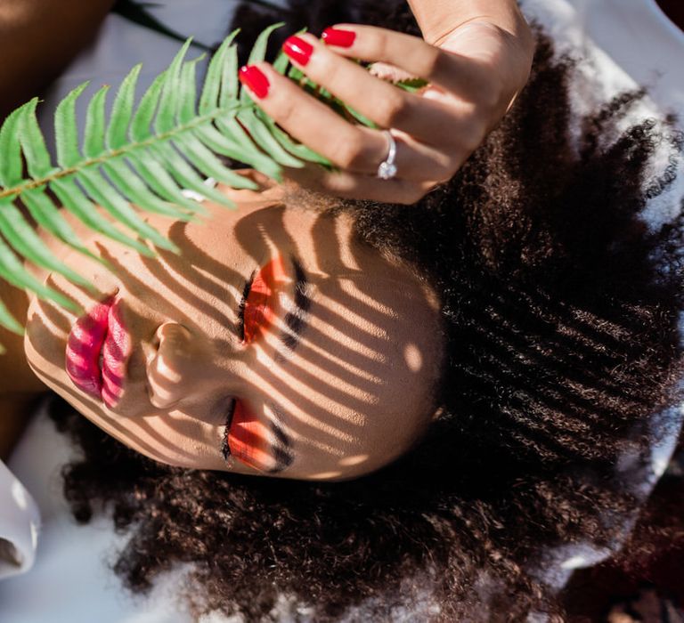 Bride with orange eyeshadow, pink lip and fern plant shadowing her face