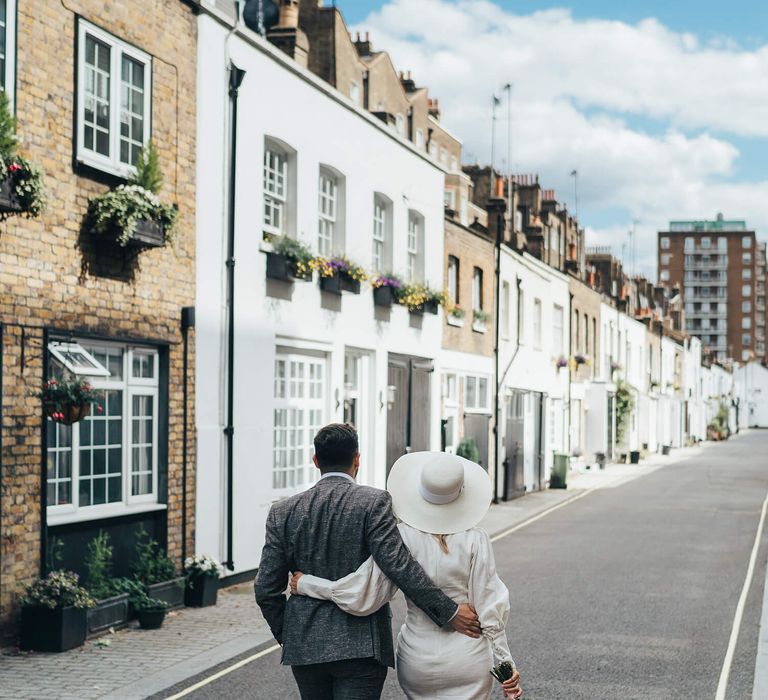 Bride and groom holding each other as they walk down a London street, bride wears short wedding dress