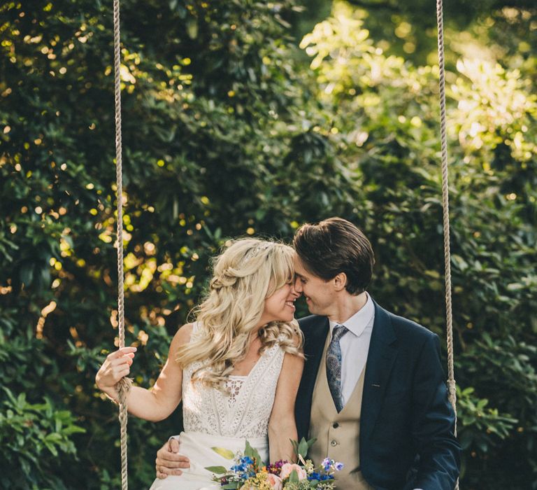 Bride holding colourful bouquet hugging groom on swing in the grounds at Iscoyd Park wedding reception 