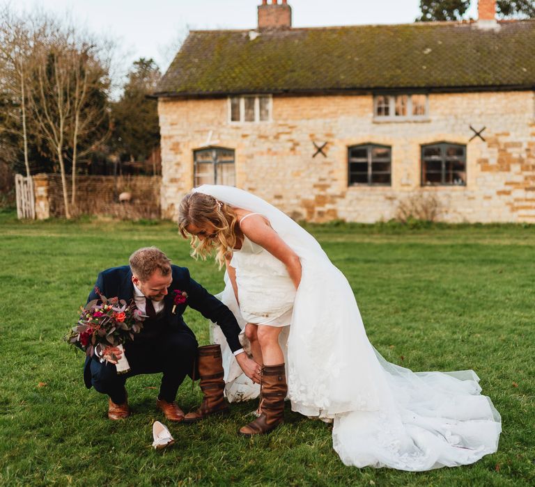 Groom helps bride put on boots to stand outside 