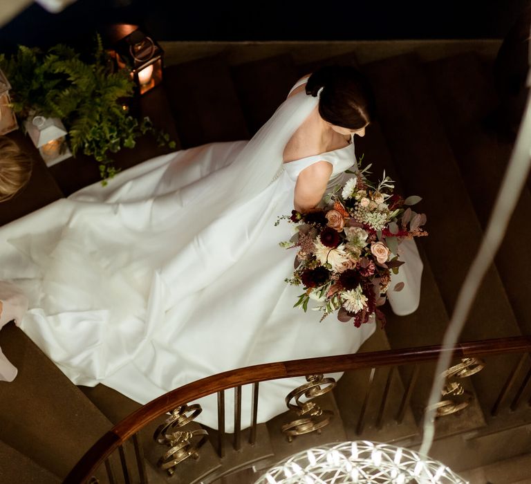 Bride walking downstairs with her bridesmaid holding her chain 