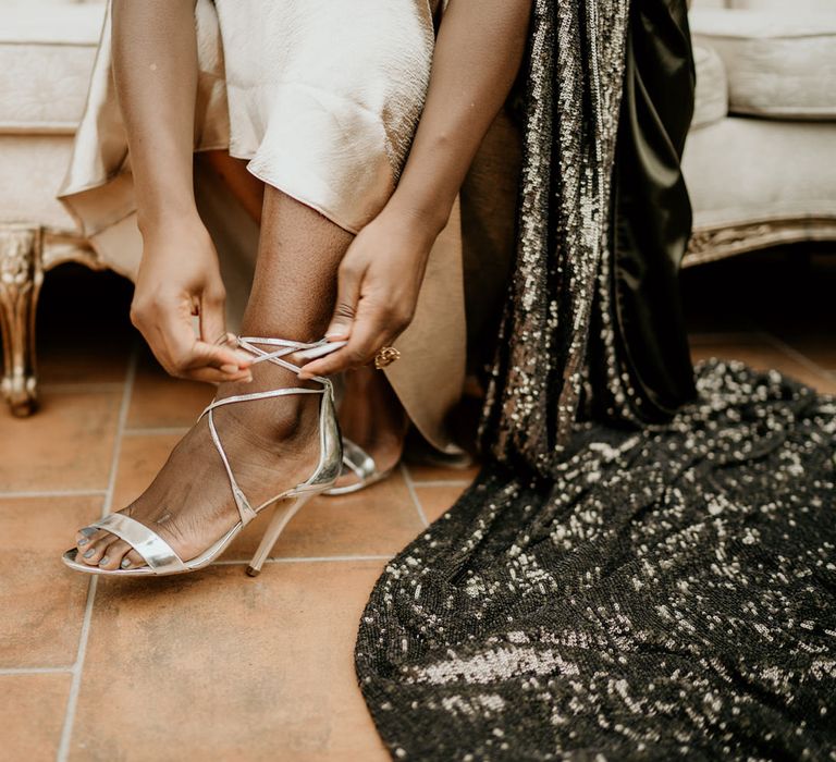 Bride with silver toe polish putting on her silver sandal wedding shoes 