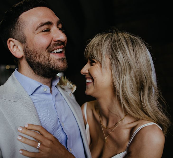 White bride with blonde wavy hair and white groom with dark hair laughing and holding on to each other