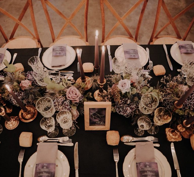 Starry night constellation table details with purple floral centrepieces, purple tapered candlesticks and purple napkins