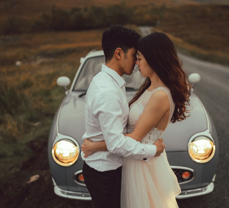 Couple embrace with vintage car in the background in Scotland