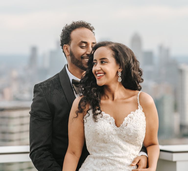 Stylish bride and groom in a black jacquard tuxedo and bride in a fitted lace wedding dress with thin straps at Ethiopian wedding 