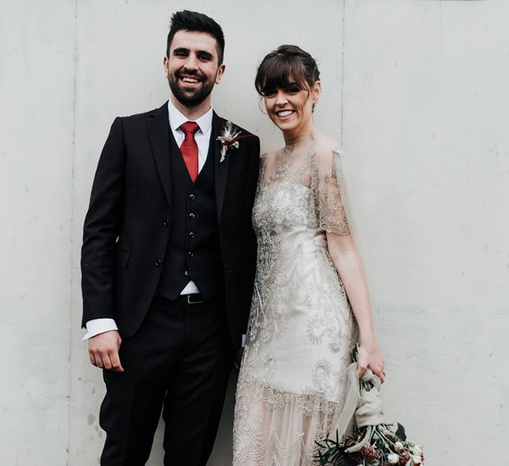 A bride and groom stand side by side, She holds an oversized homemade wedding bouquet.