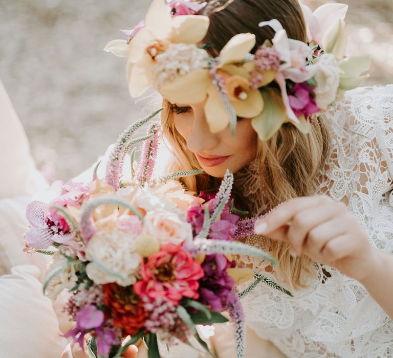 Bride in lace boho wedding dress and flower crown smells wedding bouquet of pink, white and green florals at enchanted forest wedding