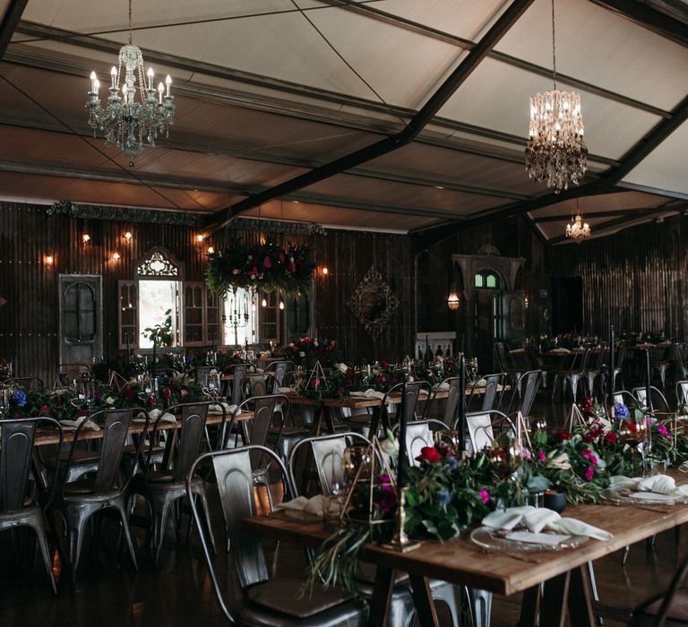 Rustic chic banquet table set up with moody romantic florals, foliage centrepieces and chandeliers