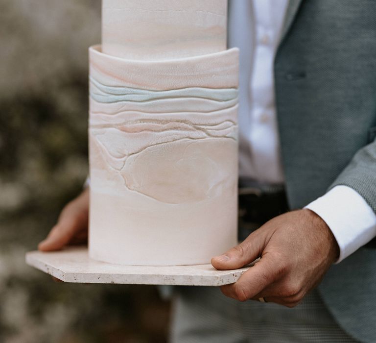 Groom holds contemporary wedding cake with pastel colouring