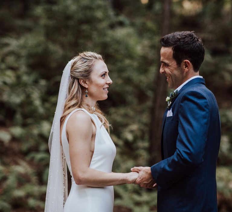 Bride & groom hold hands and look lovingly at one another during elopement ceremony in the forest