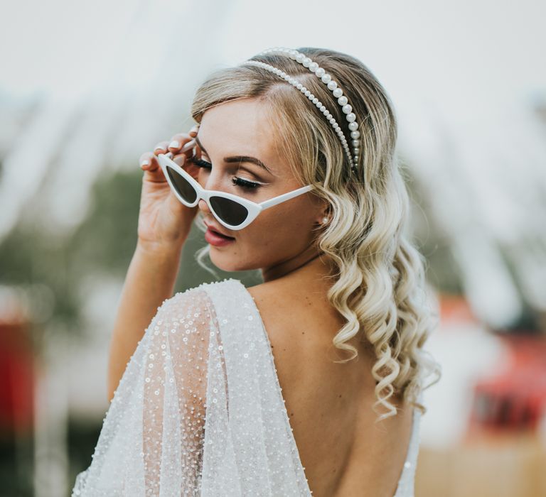 Bride in a low V back sparkly wedding dress and double pearl headband with white winged eyeliner and white cat-eye sunglasses 