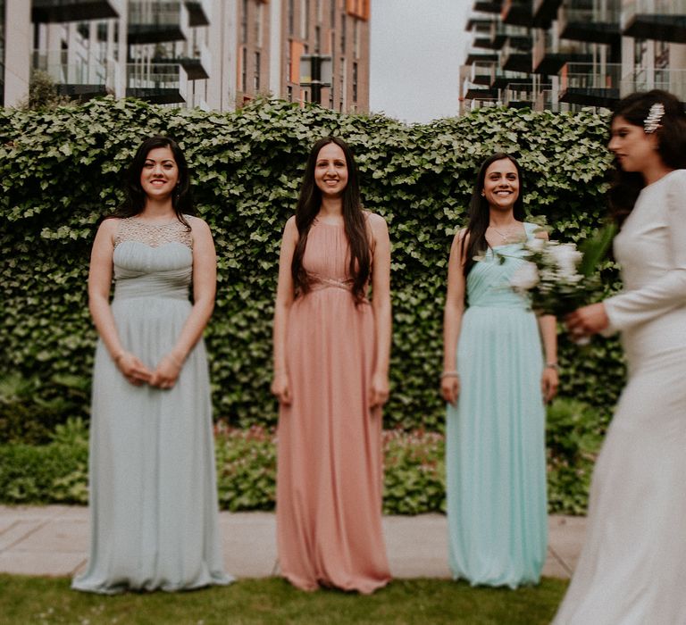 Bride in a fitted wedding dress from the high street walking past her bridesmaids in different coloured dresses 