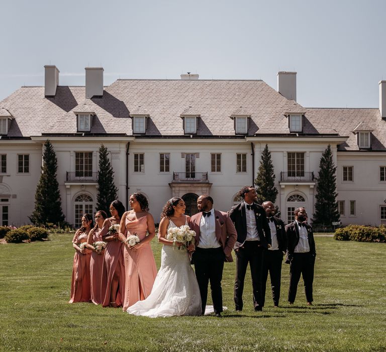 Bride & groom stand with their wedding party outdoors as the sun shines upon them