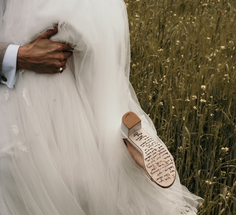 Bride walks through fields in her wedding gown and shows off hand-written poem on the bottom of her shoes from groom