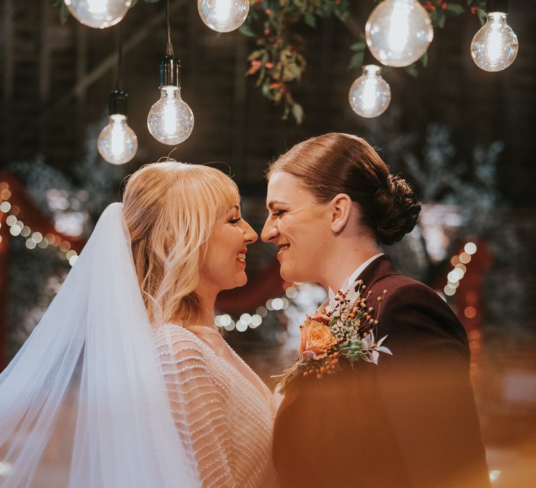 Two brides looking into each other's eyes, with the bride's orange tipped veil covering part of the camera lens