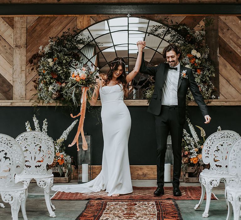 Bride and groom celebrating at the altar with a mirror backdrop and orange, white and green flower arrangements decorating the ceremony 