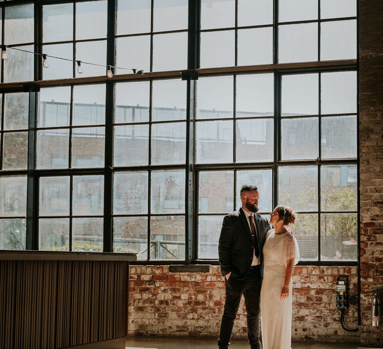 Bride & groom stand in front of large industrial style window at the Boiler Shop Newcastle