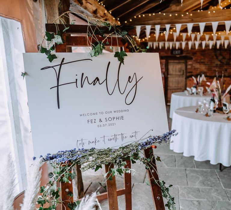 Rustic barn wedding venue complete with white sign surrounded by florals