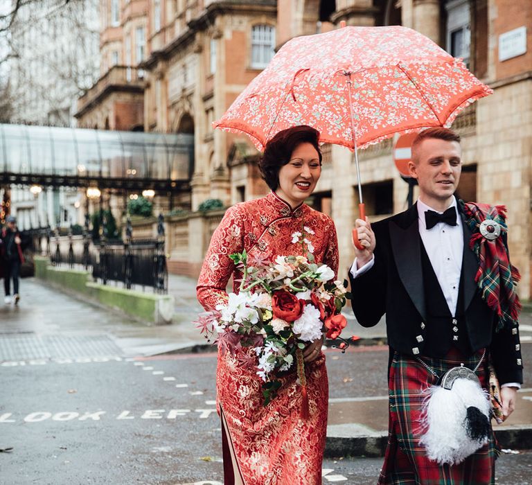 Bride and groom walk through the streets of London under red umbrella