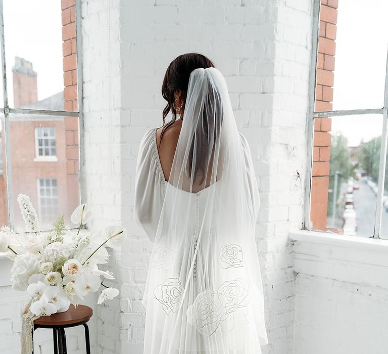 Floaty wedding dress with button details on the back wearing a fingertip length veil embroidered with roses 