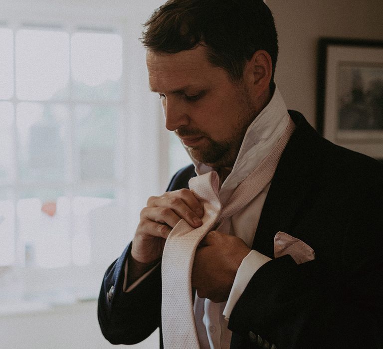 Groom on the wedding morning putting on his light pink waffle effect tie