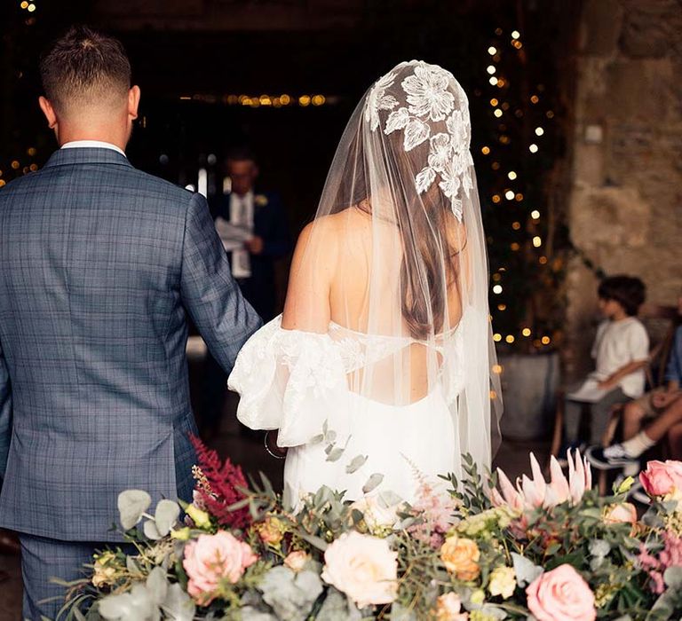 Bride in a strapless wedding dress with lace and puff sleeve detail matching her wedding veil standing next to her husband 