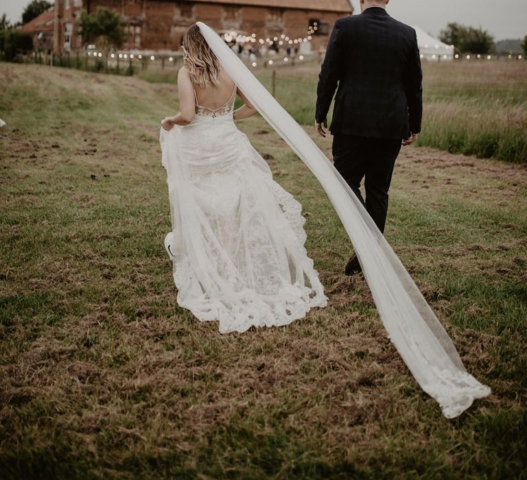 Bride walks through field on her wedding day as her veil trails behind her