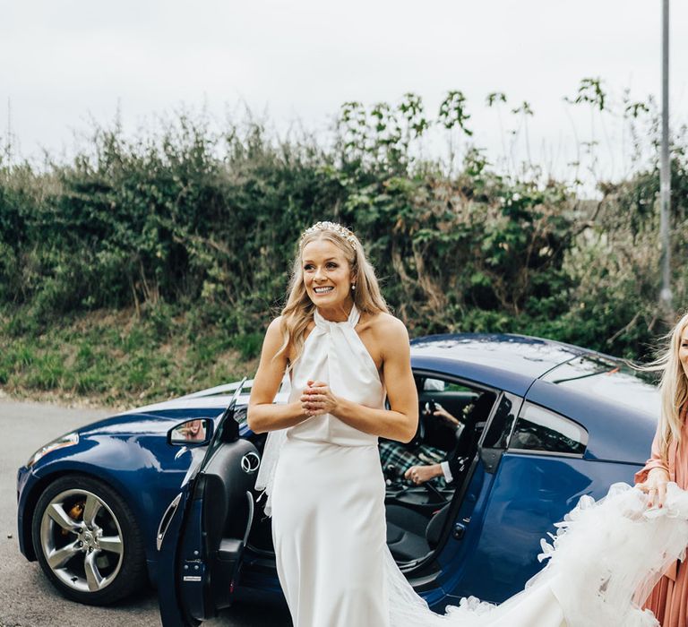 Bride in halterneck Halfpenny London wedding dress and veil walks out of car towards church before wedding ceremony 