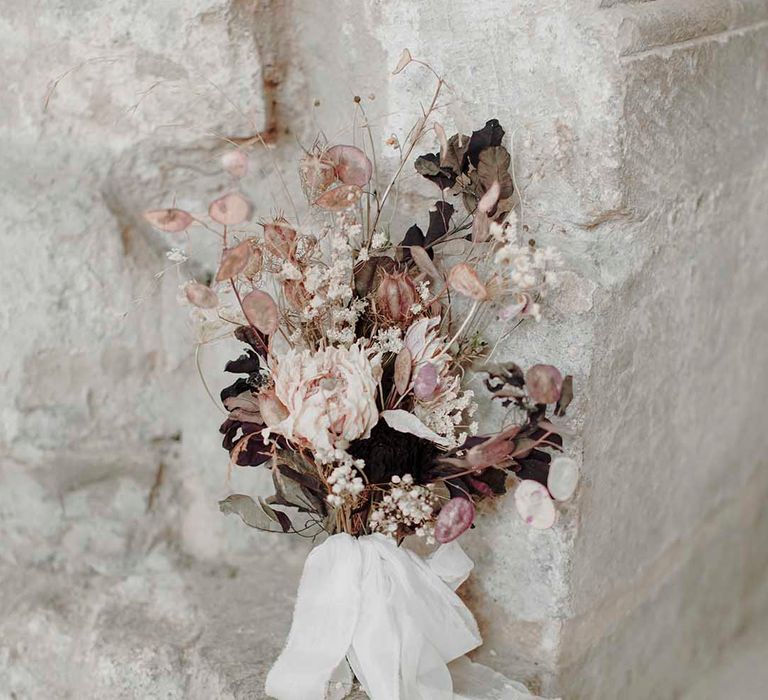 dried flower stem wedding bouquet in neutral and blush tones resting against a wall