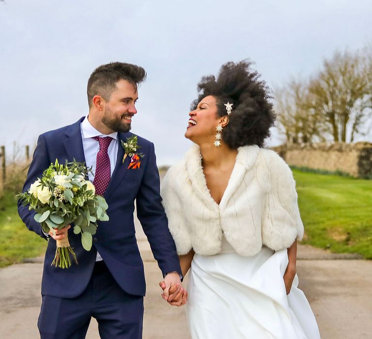 Bride & groom walk hand in hand on their wedding day as groom holds his brides bouquet