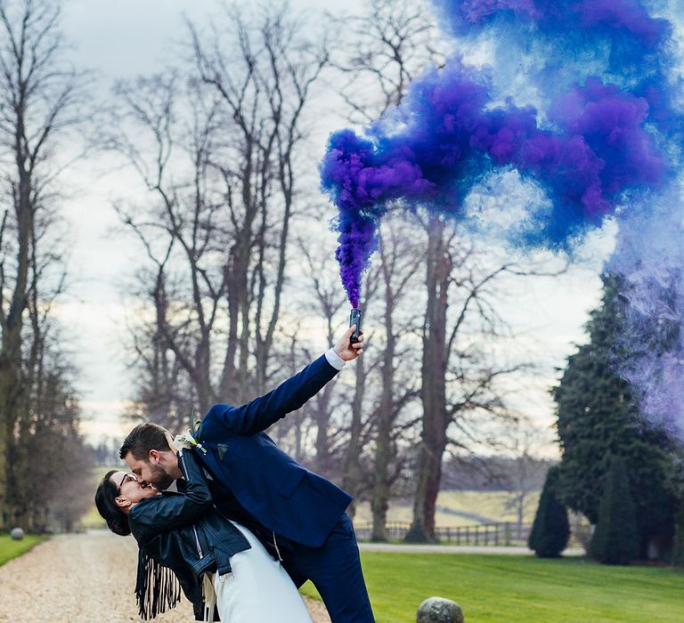 Groom lifts smoke bomb above his head as he dips back his bride and kisses her