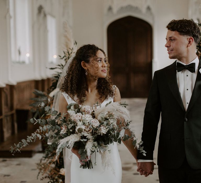 Bride & groom hold hands as they look lovingly at one another during wedding ceremony