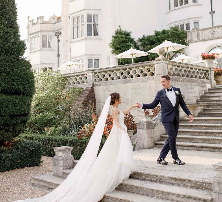 Groom leads his bride up grand staircase outdoors at Danesfield House