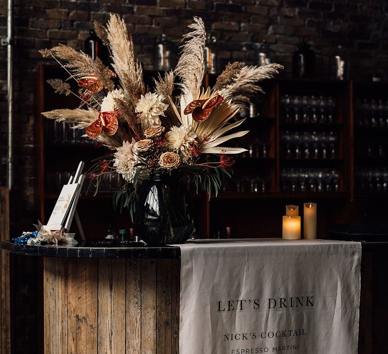 Fabric bar menu sign and dried pampas grass, anthurium and dahlia wedding flower arrangement 