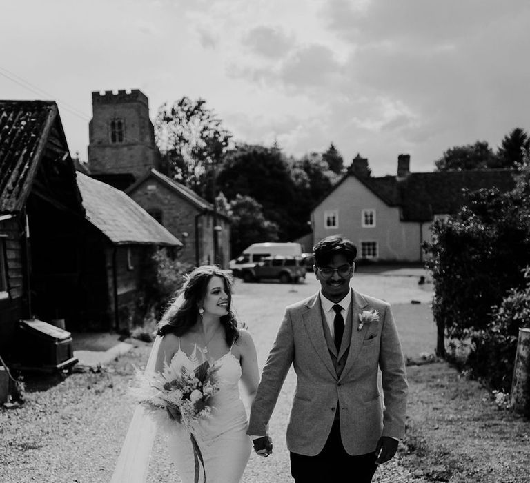 Bride & groom walk hand in hand on their wedding day as bride holds dried floral bouquet