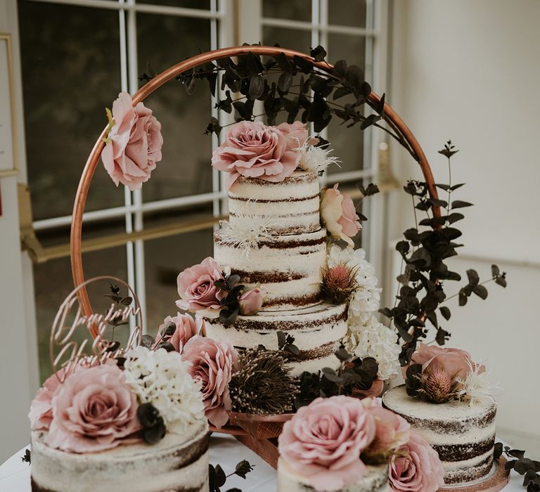 Table complete with four naked wedding cakes with white frosting and covered in pink roses 