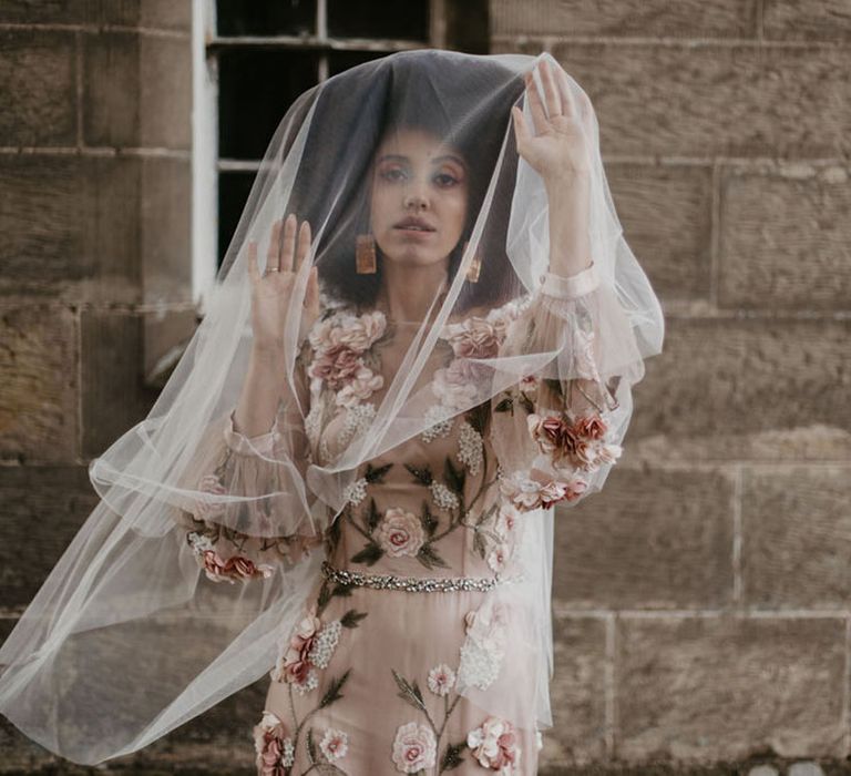 Black bride with afro hair wearing a pink embroidered wedding dress, clay earrings and veil over her face 